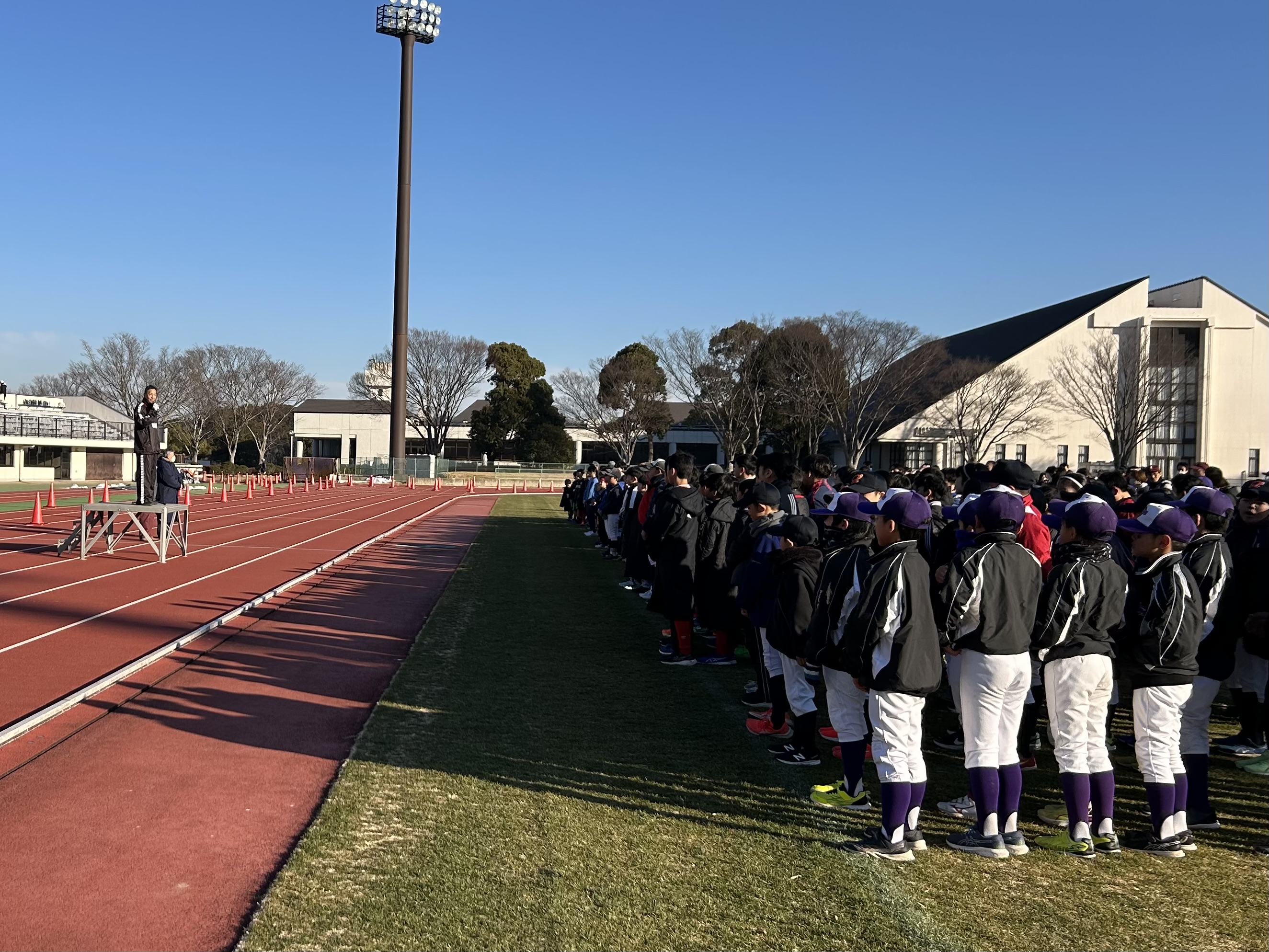 開会式の写真。成田市スポーツ少年団本部長が大勢の子どもたちの前で挨拶している様子が写っている。