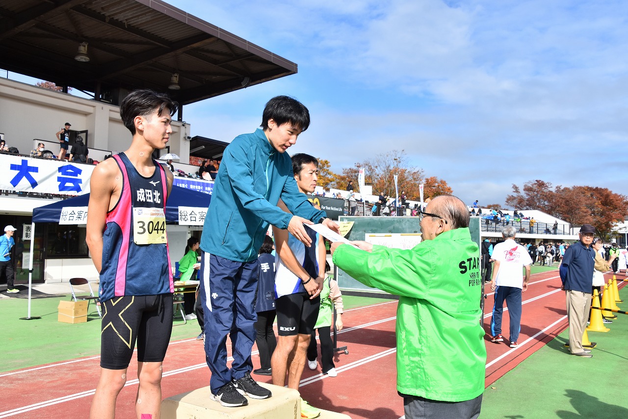 表彰式の様子。表彰台の上に立つ1位のランナーに対し、小泉市長が賞状を授与している。