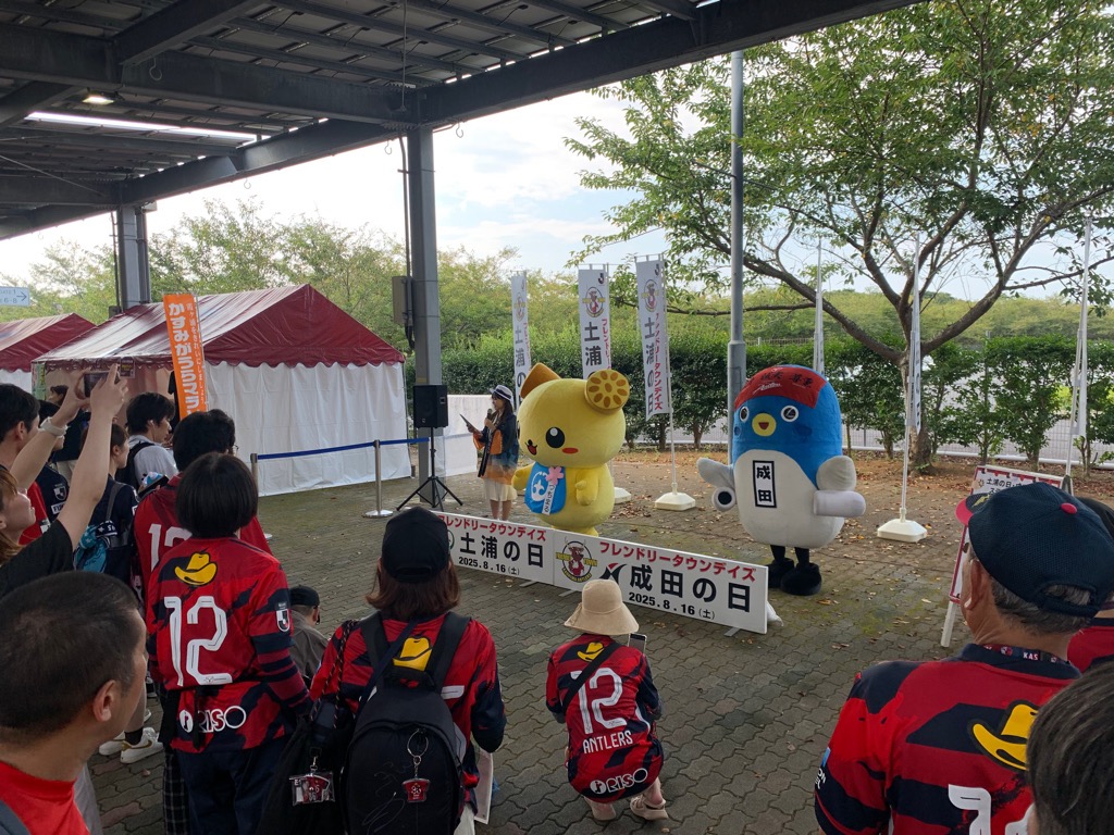 会場内の特設ステージに「うなりくん」と「つちまる」が登場した時の写真。ステージの周囲には鹿島アントラーズのユニフォームを着た人の人だかりができ、それぞれ写真を撮影している。