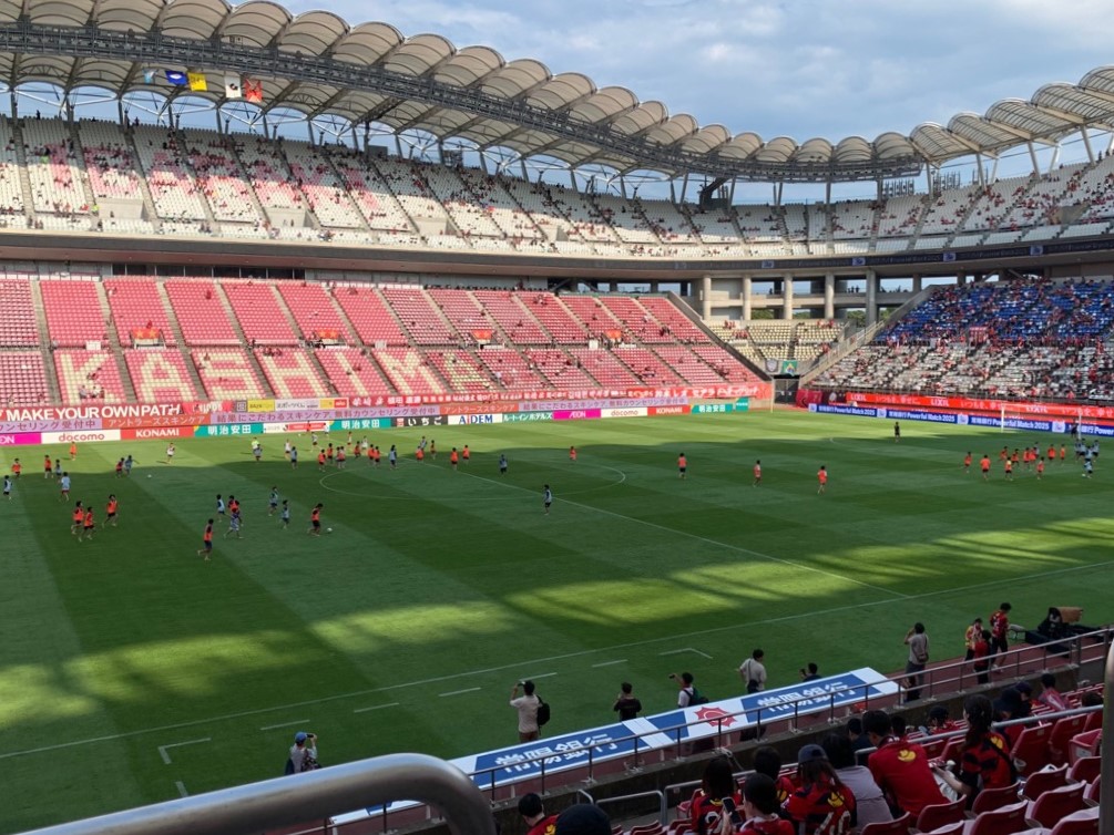 メルカリスタジアムのグラウンドで小学生がカーテンレーザーマッチに参加する様子の写真。ビブスの色でチーム分けされた小学生が裸足で芝生の上に立ち、サッカーを行っている。