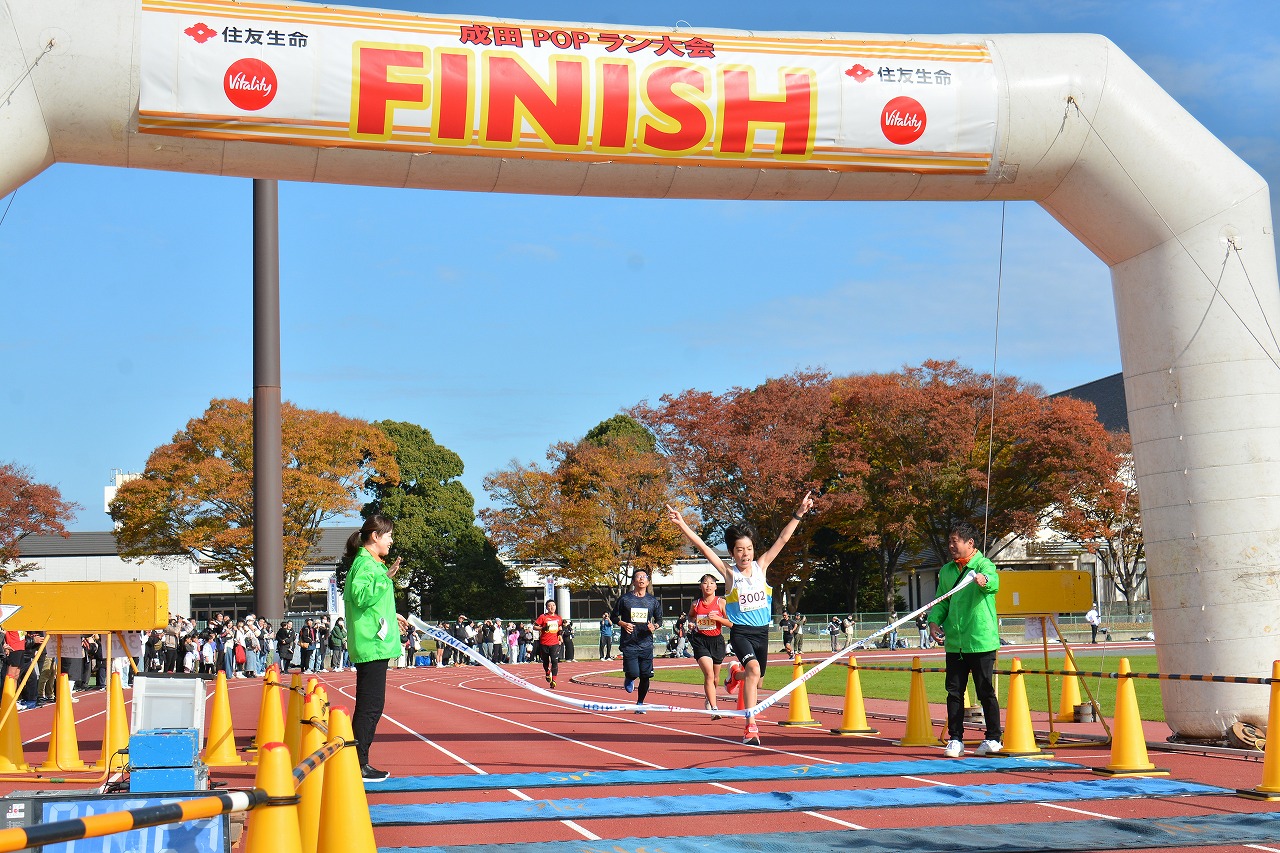 2025成田POPラン大会の3キロメートルの部に参加した小学生ランナーがゴールする様子の写真。両手を挙げてゴールテープを切っている。